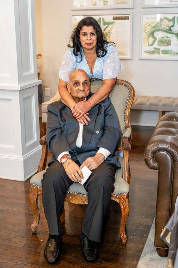 Renu Bhardwaj standing behind her seated father with her hands resting on his shoulders.